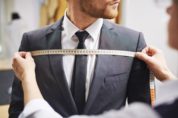Massschneider Info Massschneider misst mit einem Massband die Brustweite eines jungen Mannes.