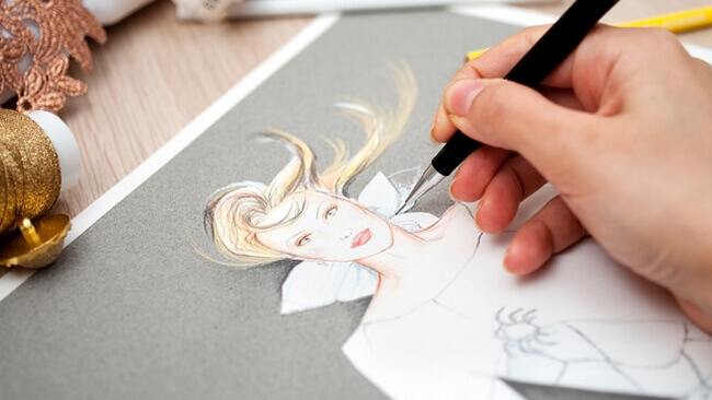 Bildausschnitt zeigt eine Hand, die einen Stift hält und damit einen Modeentwurf zeichnet
