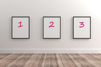 An einer weißen Wand hängen drei eingerahmte weiße Blätter, auf denen in pink die Zahlen 1, 2 und 3 stehen.